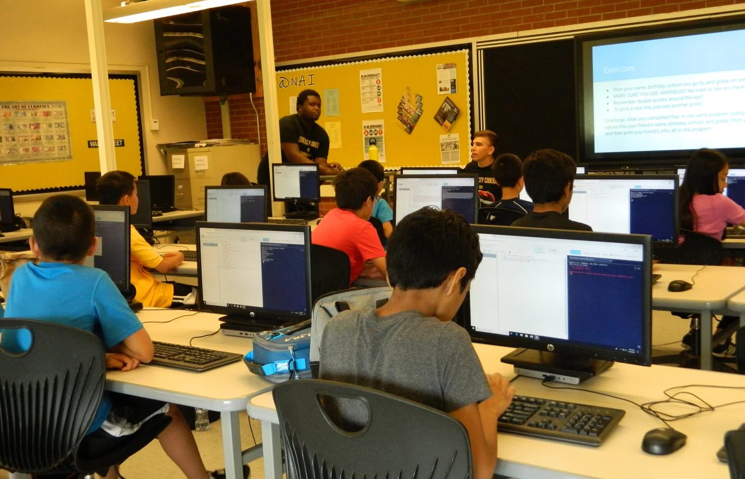 Students at a Steel City Codes summer camp writing Python at their computers while a mentor teaches.