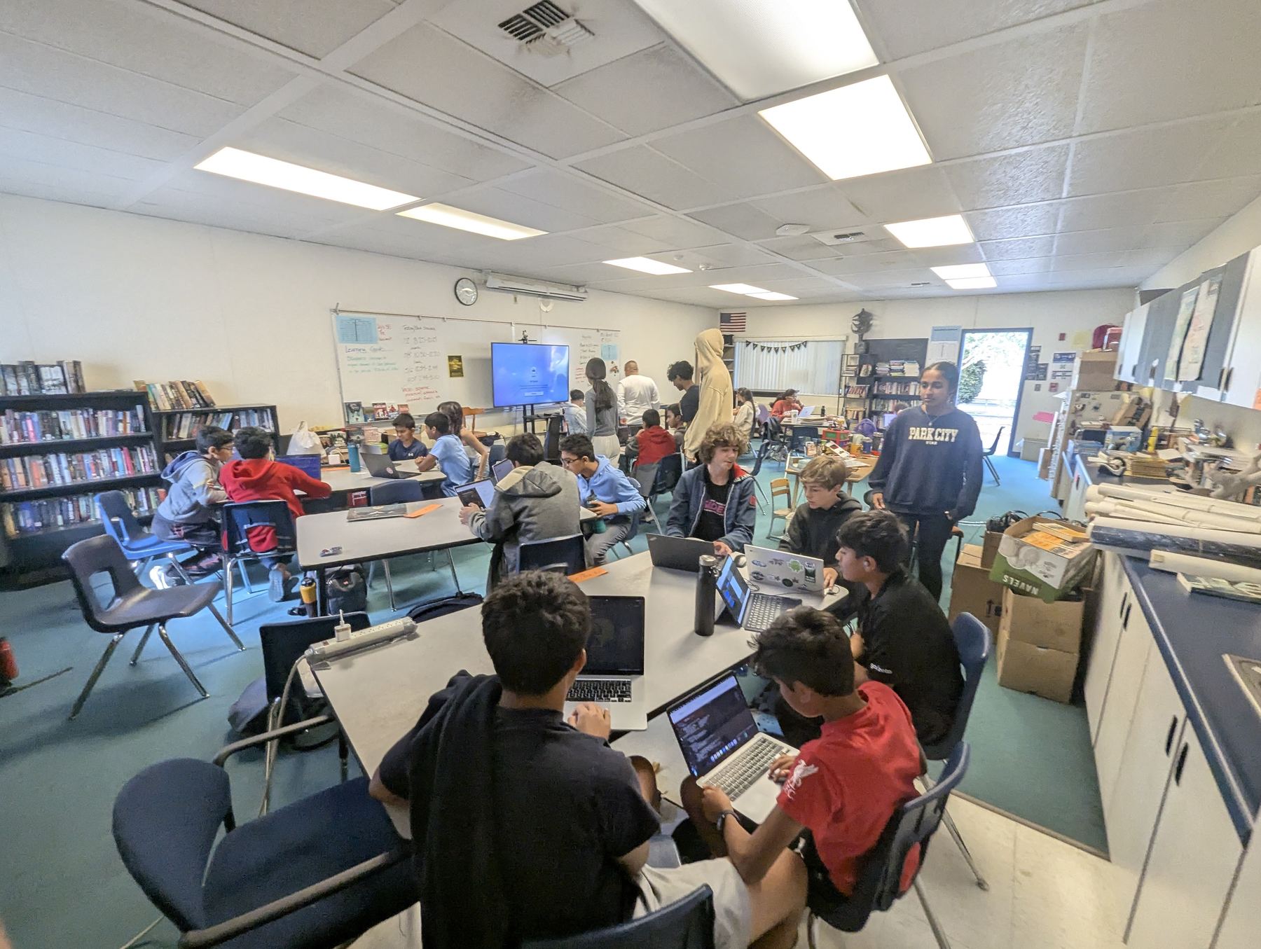 A high school mentor standing beside a table of students who are coding on laptops during a chapter session.