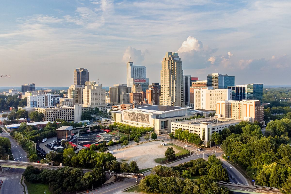 Downtown Raleigh towers above the convention center and green trees in afternoon sunlight.