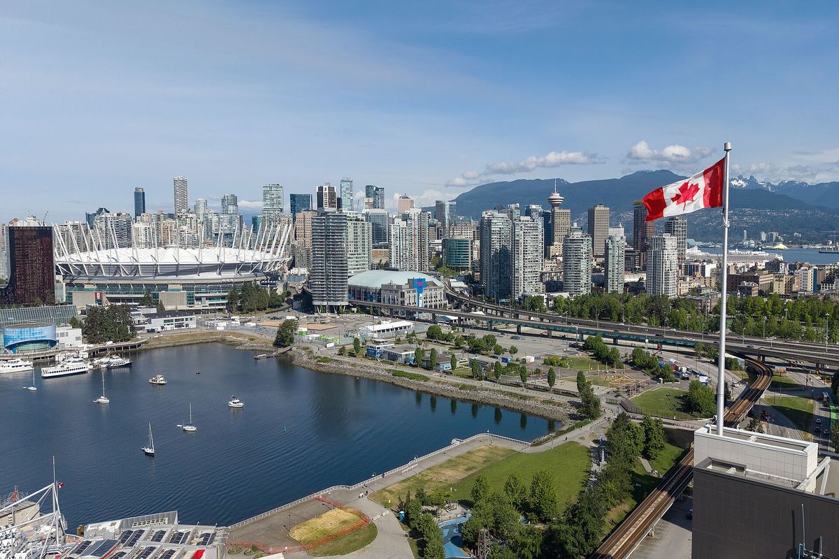 Vancouver towers and BC Place beside False Creek, with mountains and a Canadian flag in the background.